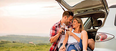 Ein Paar sitzt am Kofferraum Ihres Fahrzeugs mit einem Drink