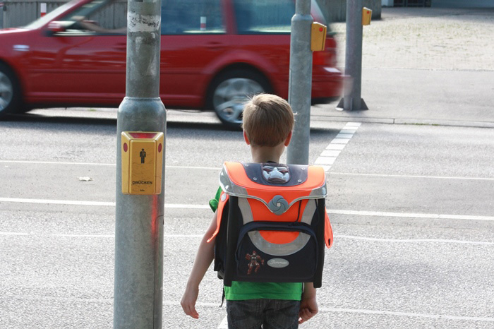 Kind steht auf dem Schulweg an einer Ampel.