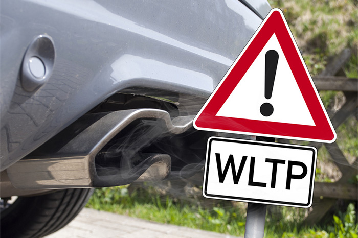 Straßenschild, "Achtung, WLTP", vor dem Auspuff eines Autos